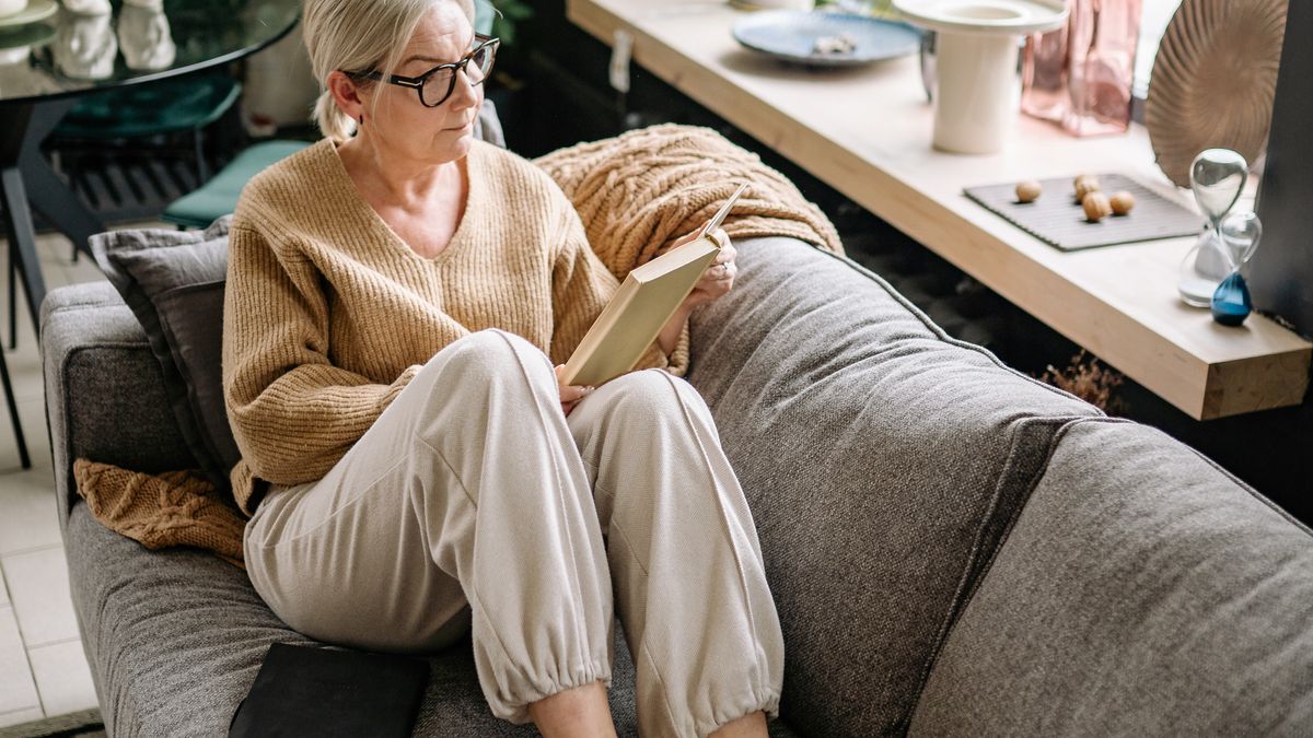 Woman in a knit sweater reading a book on a gray sofa at home